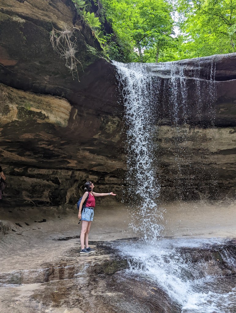 Lillian standing beside a waterfall in LaSalle Canyon in Starved Rock, reaching out and touching the water.